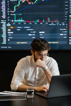 Businessman analyzing stock market data on laptop with graphs displayed. Focused and thoughtful.